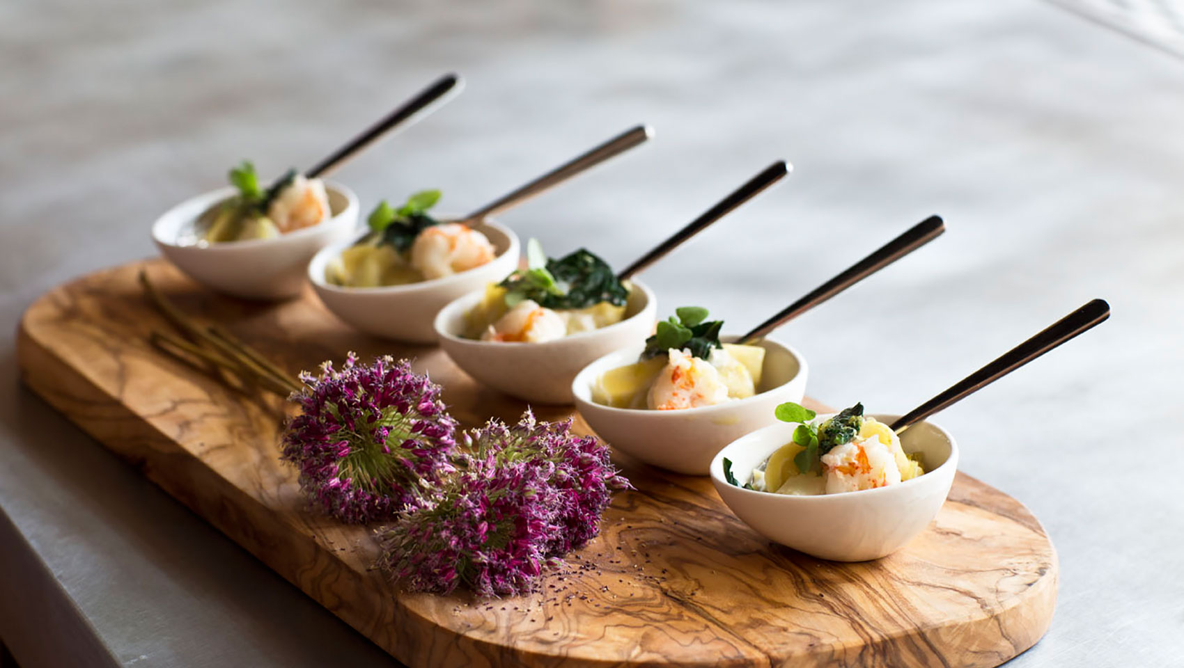 Mini bowls with catering fare placed upon wooden slab