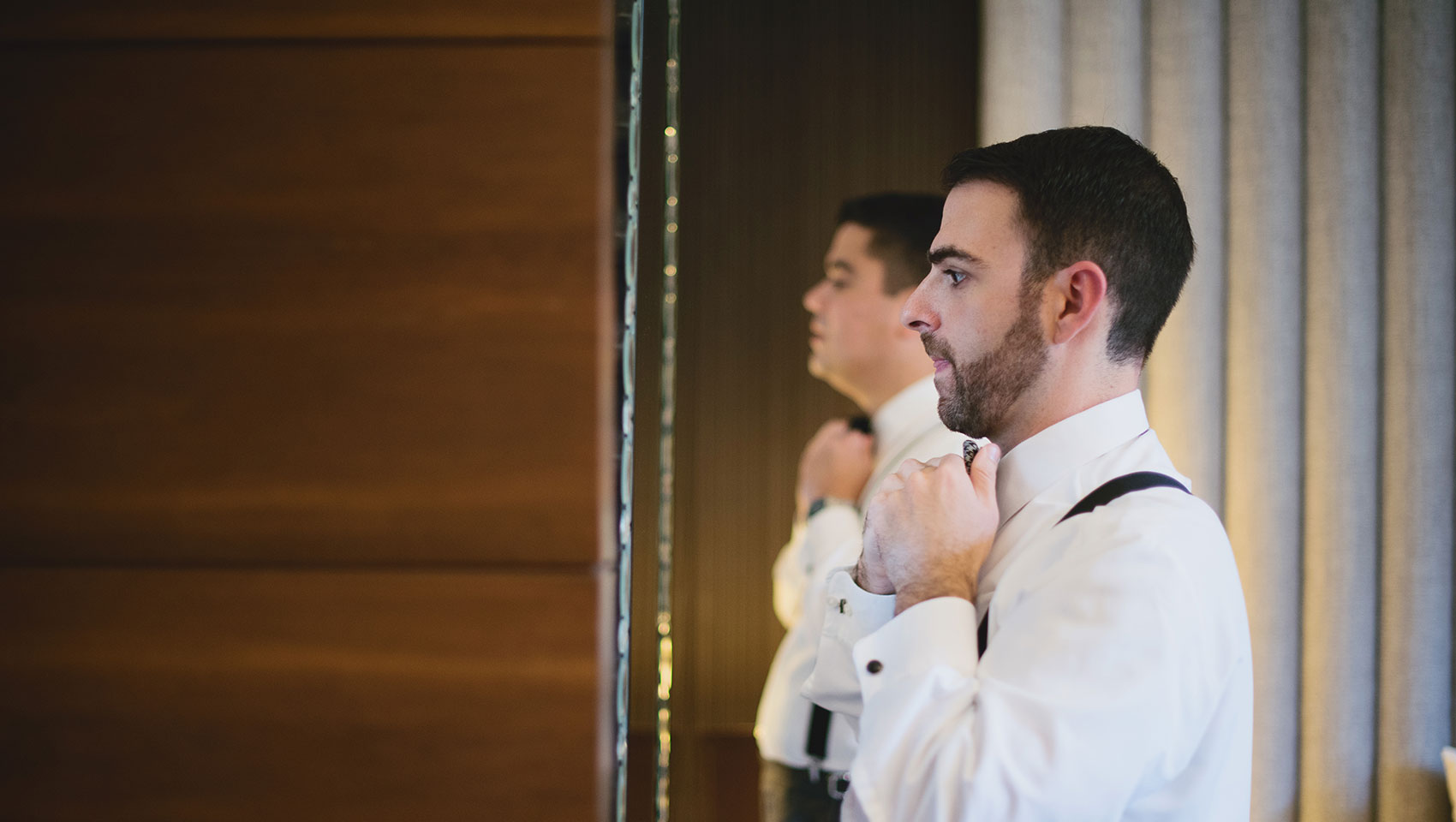 Groom adjusting his bowtie in the mirror on his wedding day